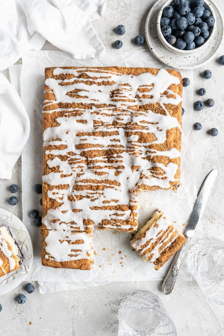 A delicious blueberry sheet cake with white icing on top with slices cut out