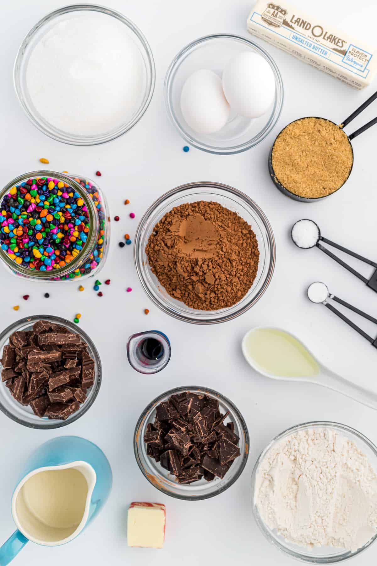 Clear bowls filled with baking ingredients like cocoa powder, sugar and rainbow sprinkles