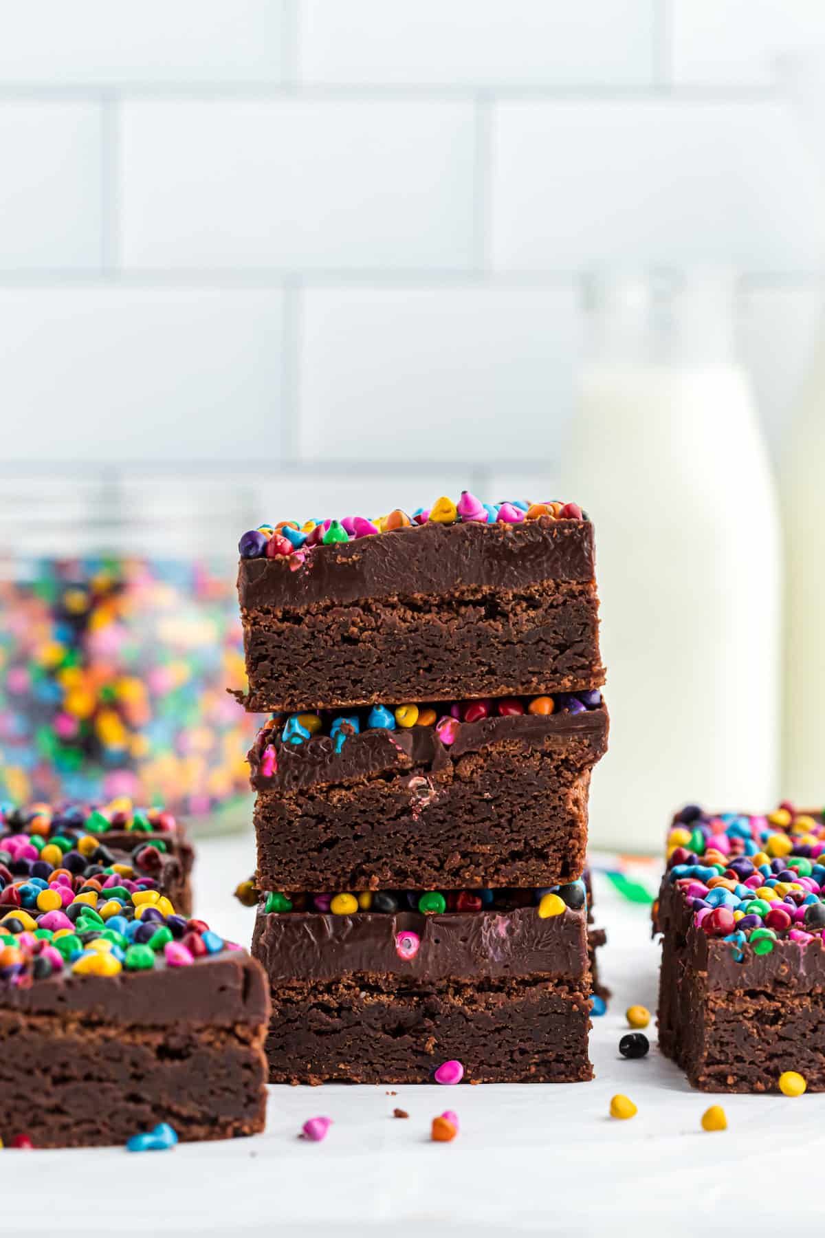 A stack of frosted brownies with colorful chocolate chip sprinkles on top