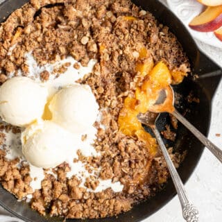 A close up of a delicious peach crisp recipe ready to serve with melting vanilla ice cream