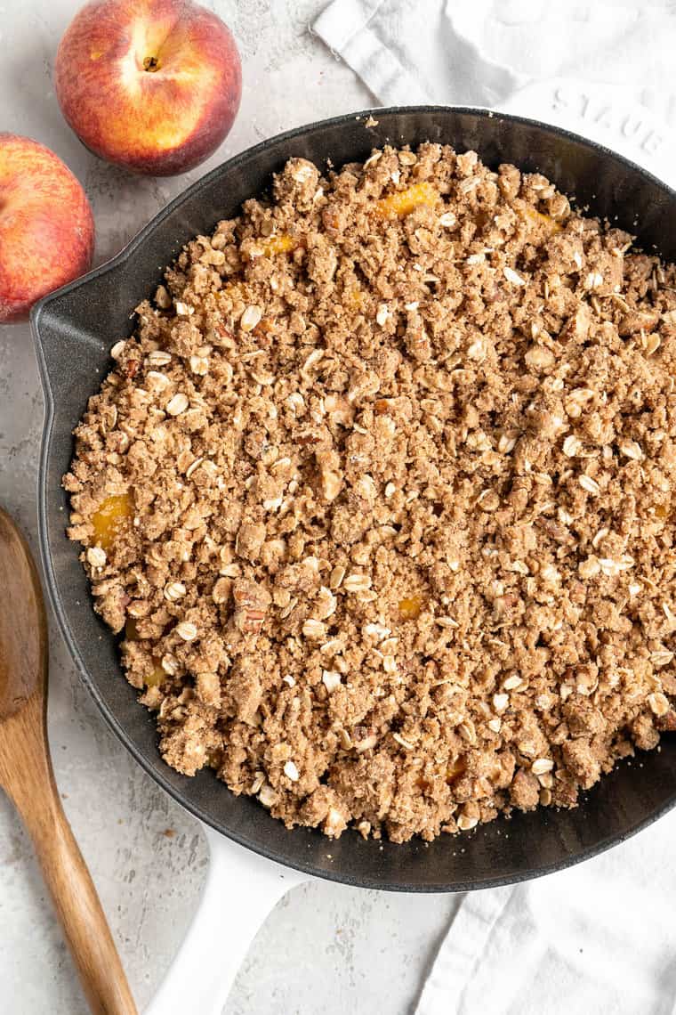A crumble oat topping poured on top of peach slices before baking