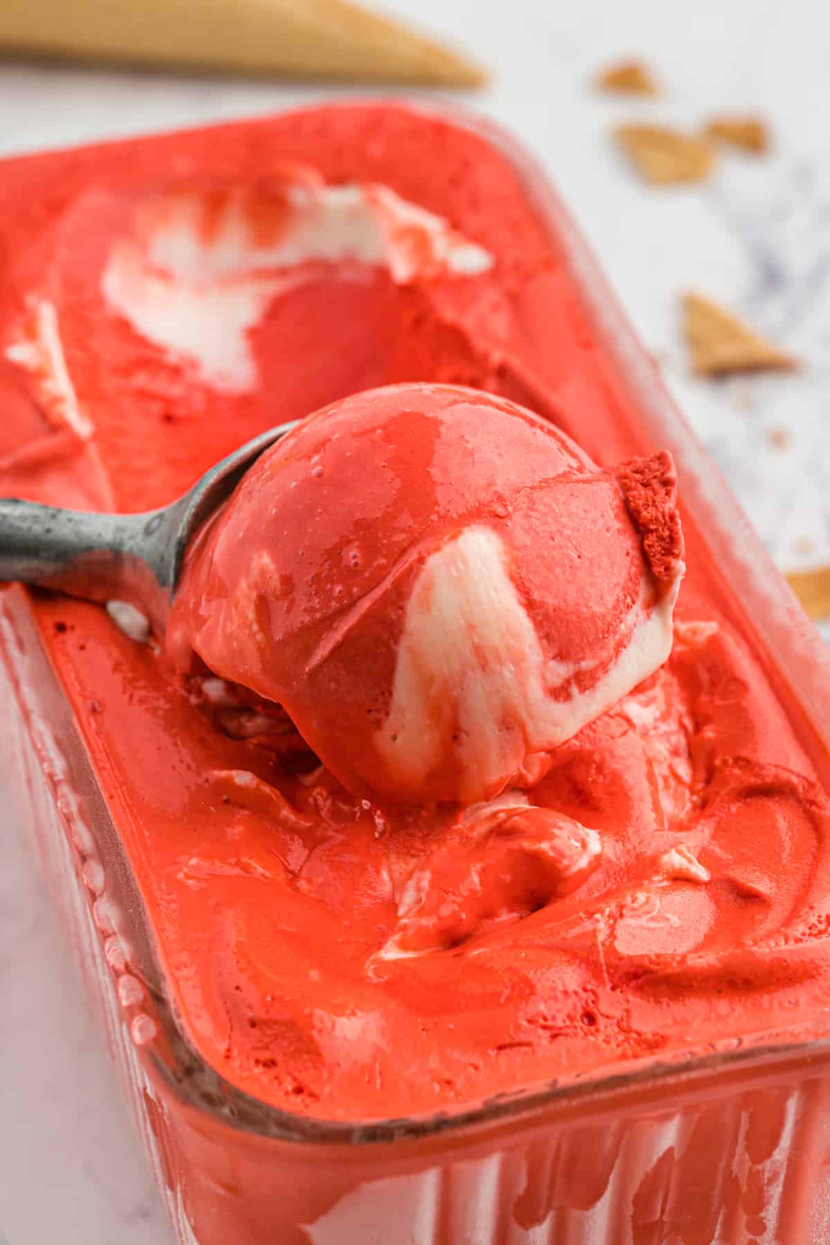 Red velvet ice cream being scooped out of canister to serve