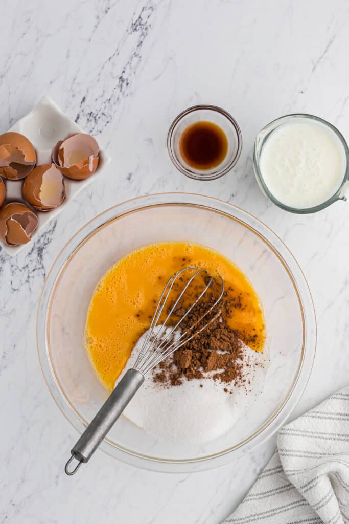 Egg yolks, cocoa powder and sugar being whisked together in a clear bowl