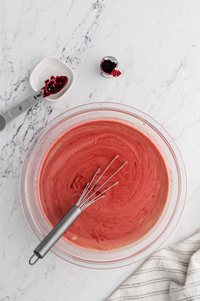 A red colored ice cream base being whisked before chilling