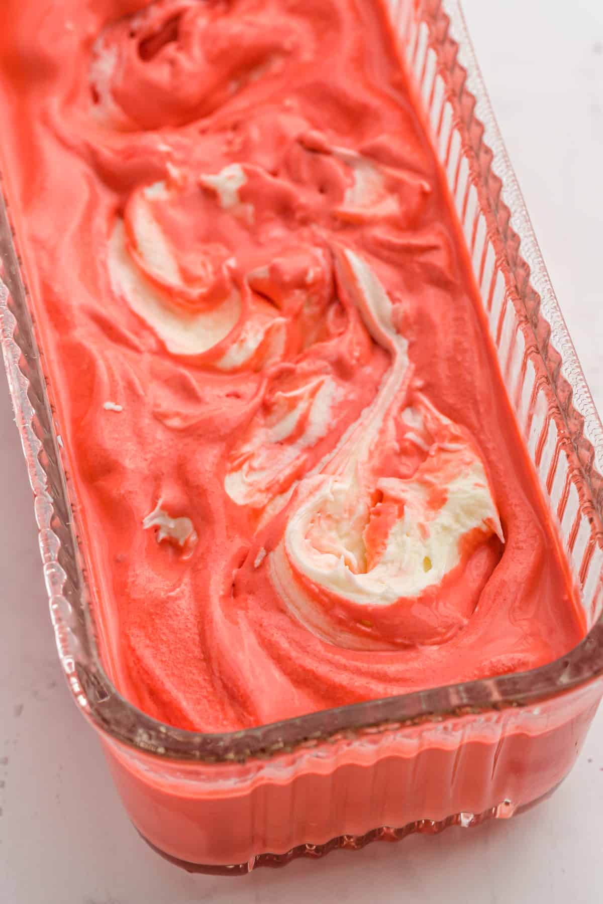 A red colored ice cream with a white swirl inside of an ice cream container after freezing