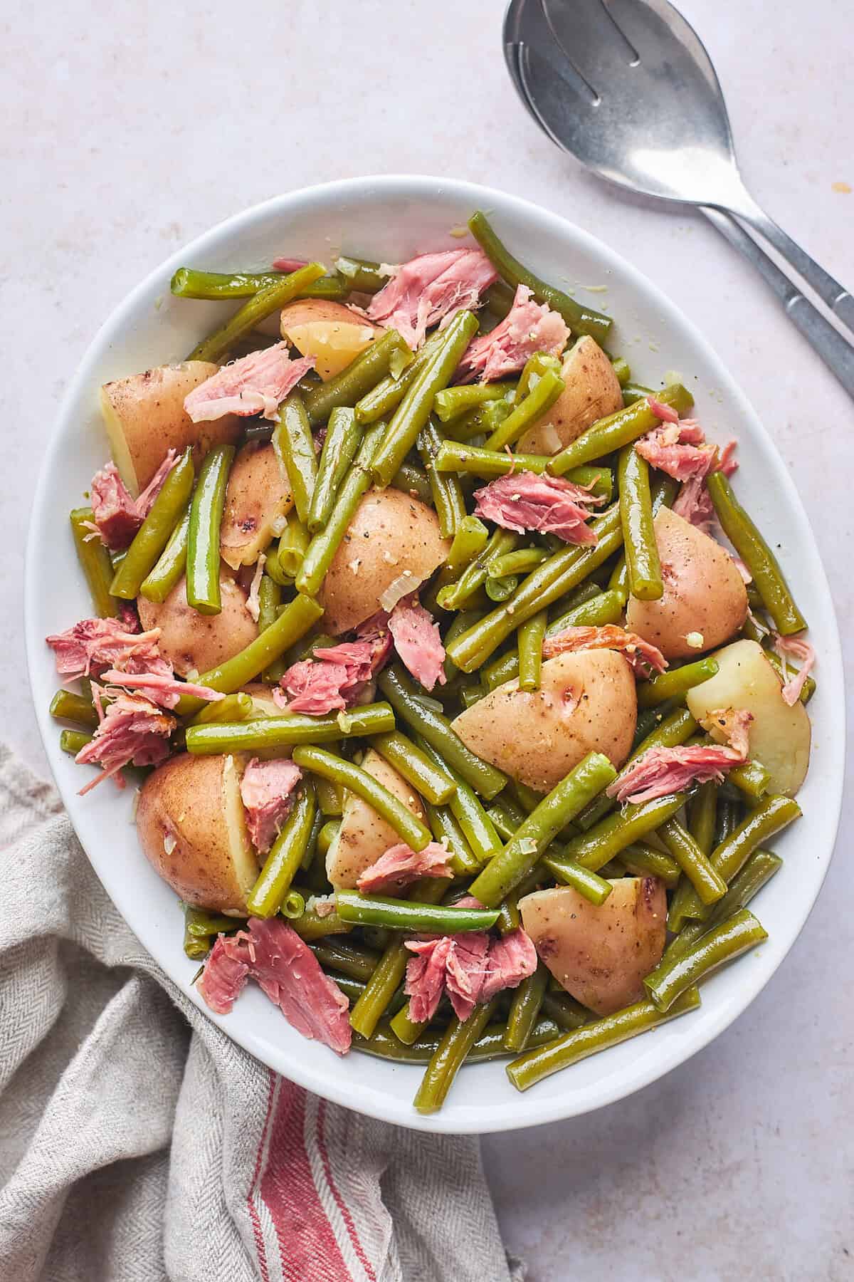 A large white platter of southern style green beans with smoked turkey and potatoes on a white background