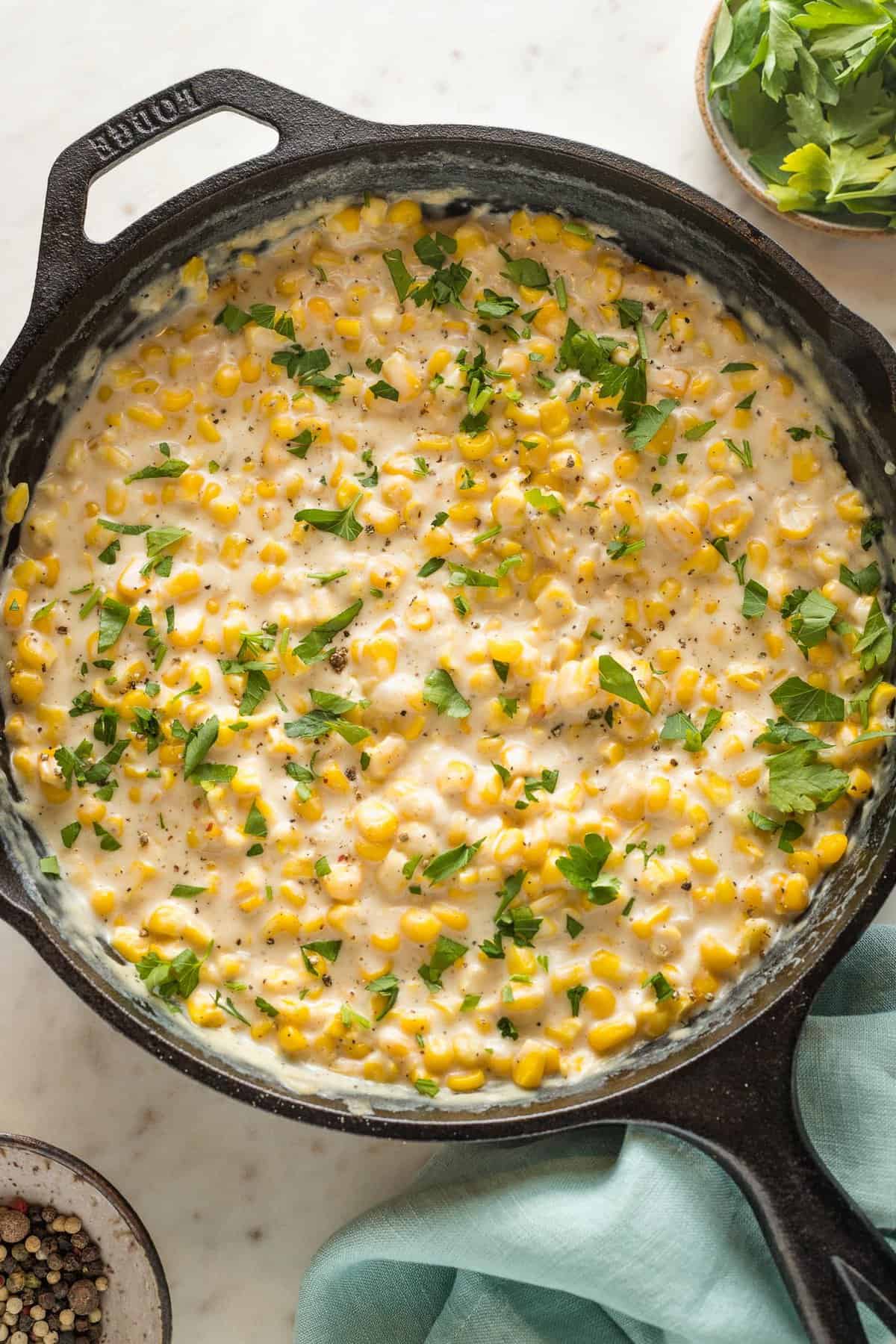 Creamed corn in a cast iron skillet with parsley leaves on top under a teal napkin