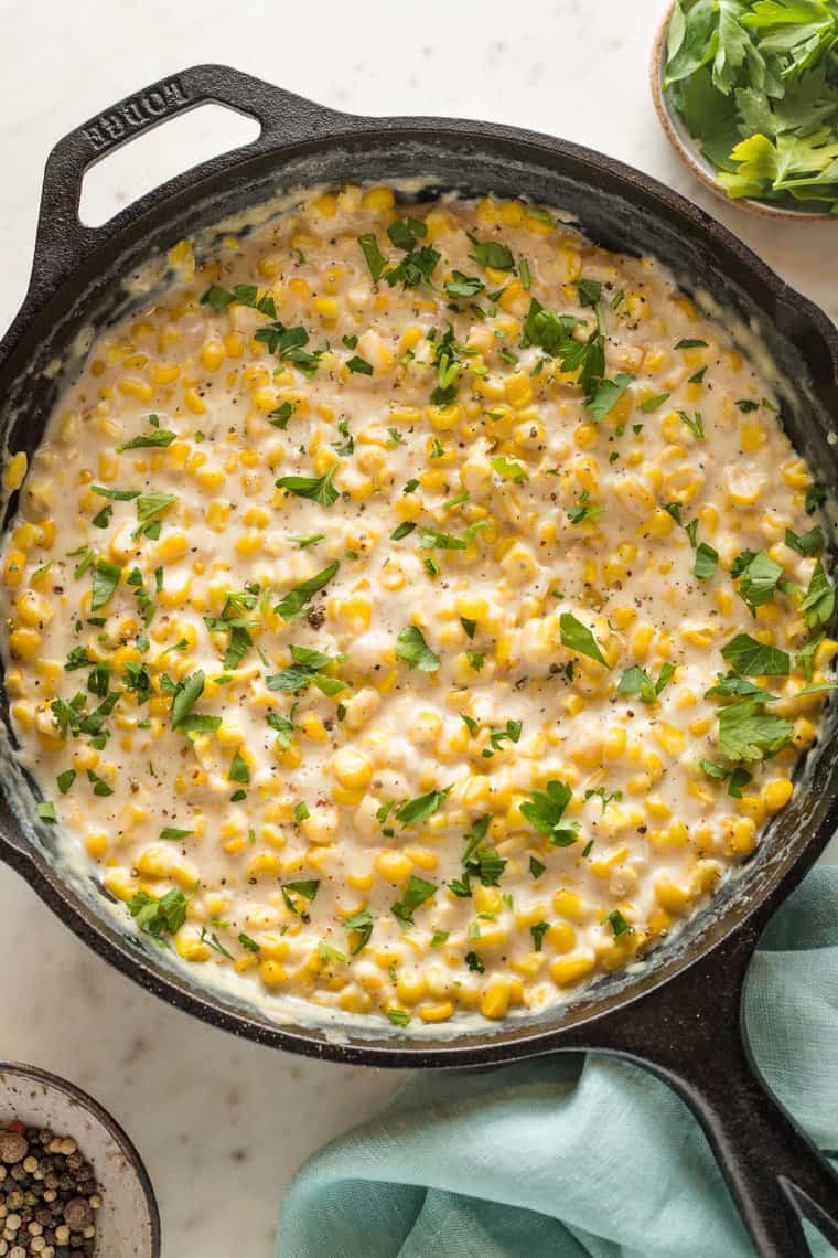 A close up of homemade cream corn in a cast iron skillet with parsley garnished on top