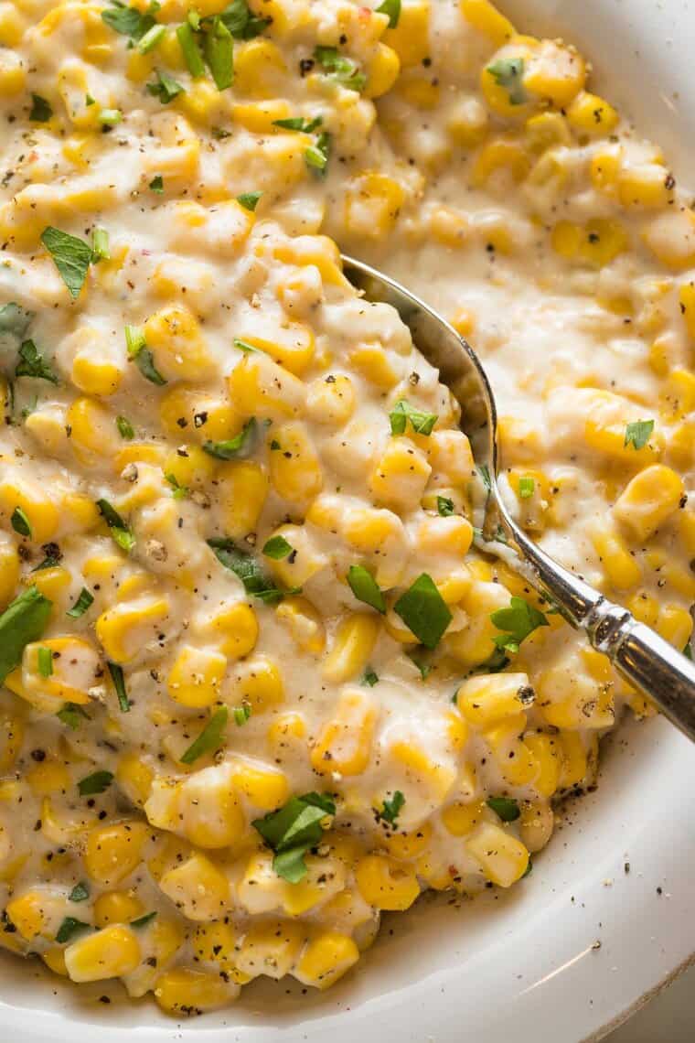 A close up of creamed corn recipe with a spoon digging in