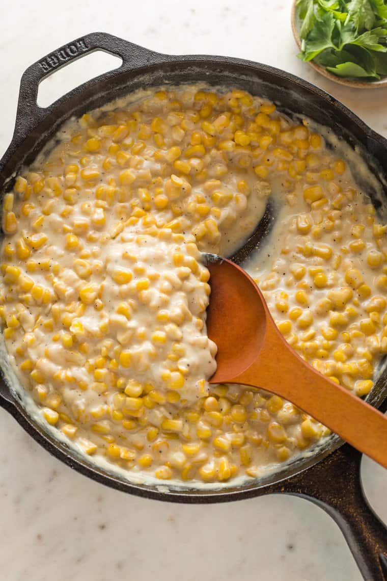 Creamed corn being stirred together with a wooden spoon in a cast iron skillet