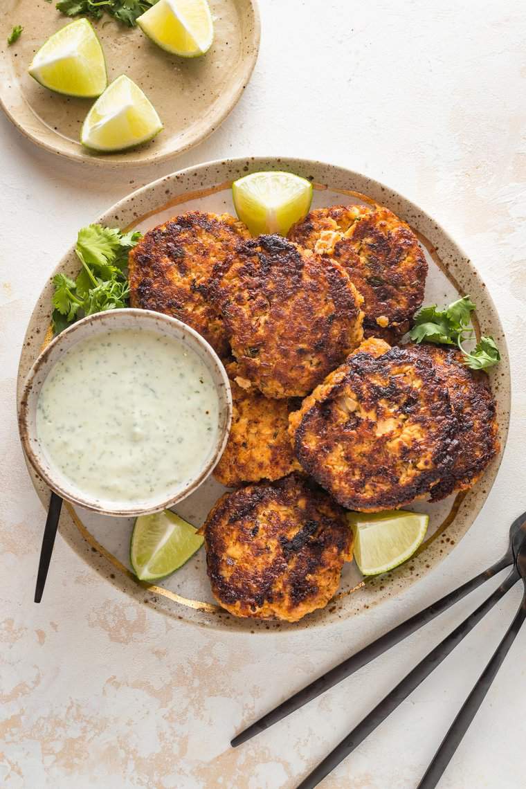 Cajun salmon patties on a plate with yogurt sauce and lime wedges for serving.