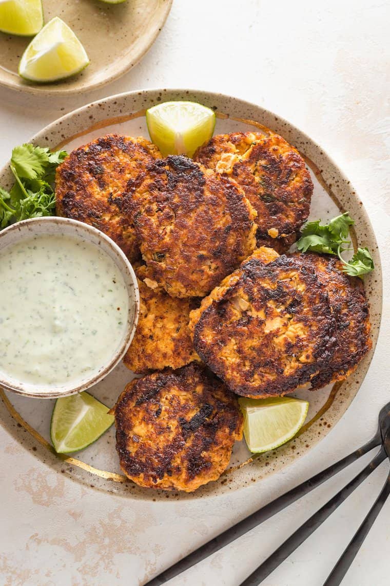 Salmon cakes on a large plate with a small bowl of yogurt sauce for serving.