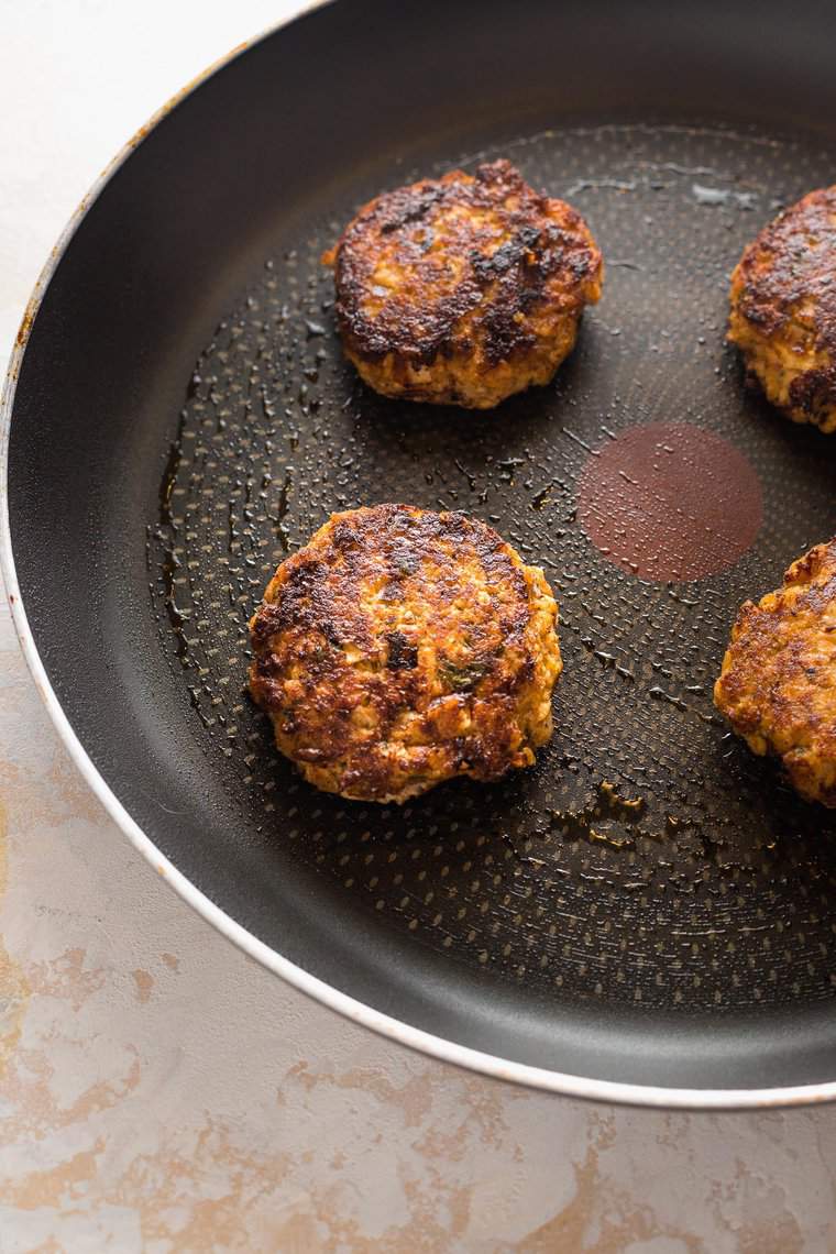Salmon patties frying in a pan before serving.
