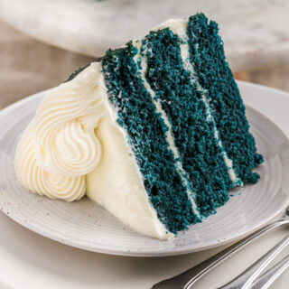 A slice of blue velvet cake on a white plate with forks nearby