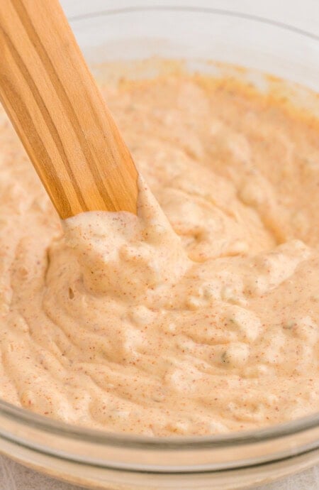 creole remoulade sauce close up in a clear bowl with wooden spoon stirring