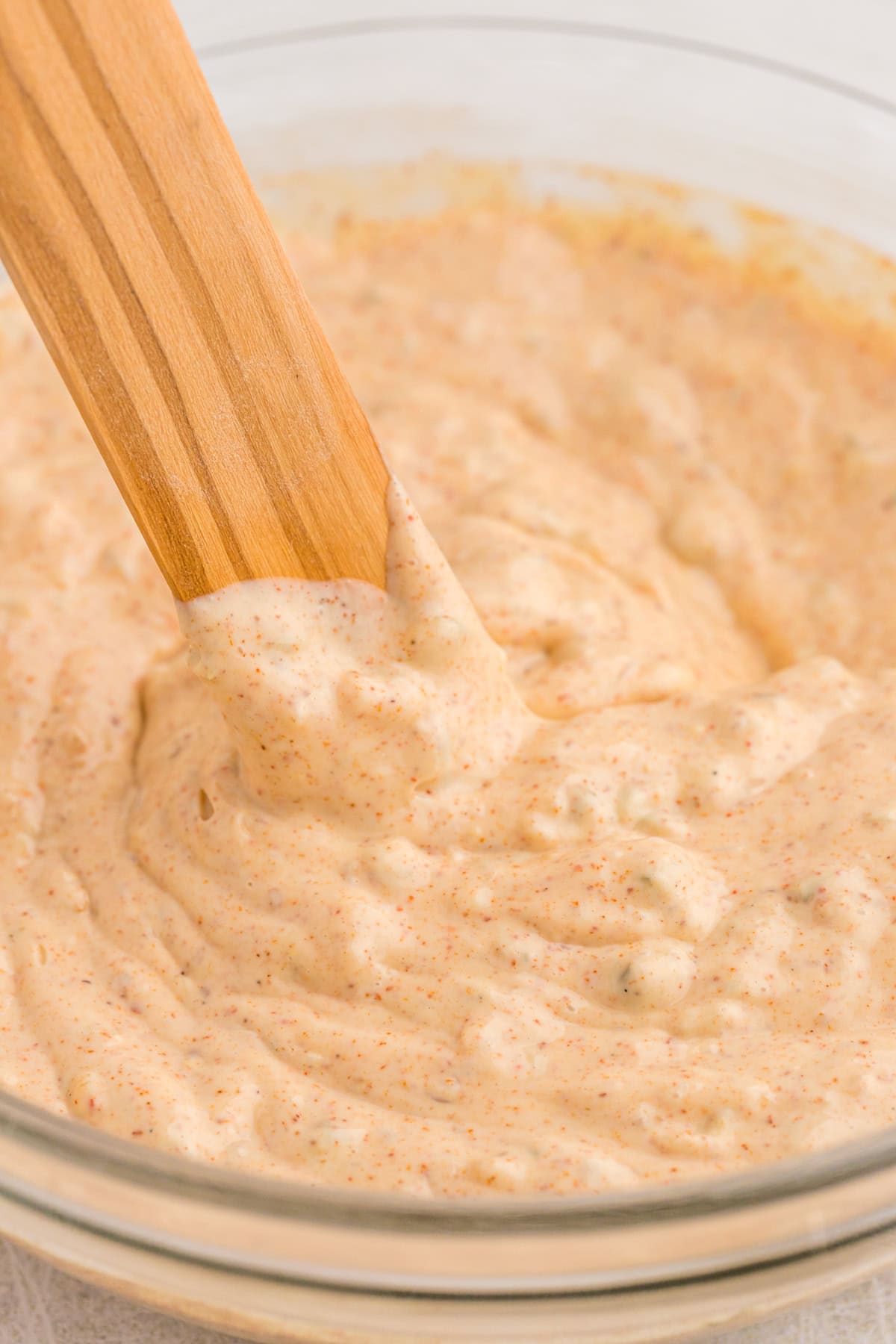 creole remoulade sauce close up in a clear bowl with wooden spoon stirring