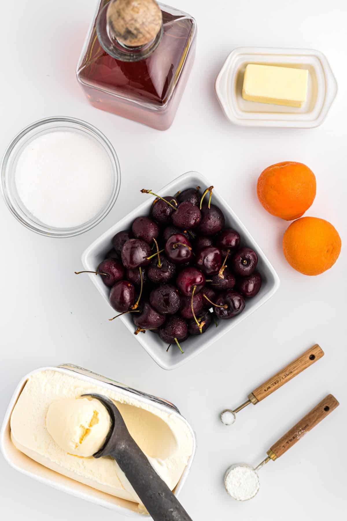 Cherries in a white rate, oranges, butter, and alcohol in separate bowls to make a cherry sauce recipe