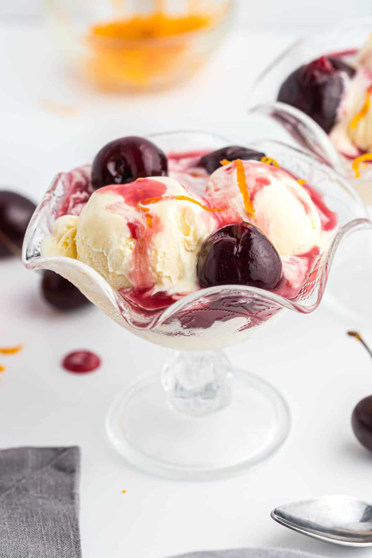 A glass bowl with cherry jubilee over vanilla ice cream with orange zest ready to serve