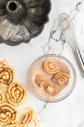 Pieces of cinnamon roll dough in a bowl filled with cinnamon sugar