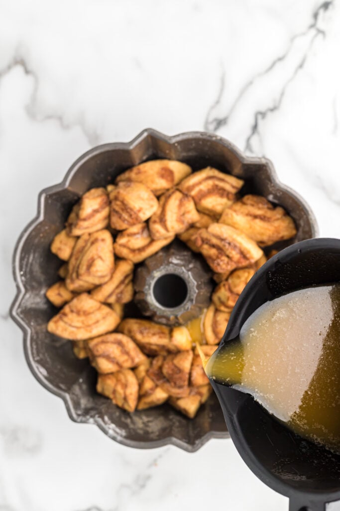 Melted butter being poured over cinnamon roll dough in a bundt pan