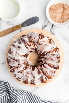 Vanilla icing poured over baked cinnamon roll dough monkey bread in a bundt pan