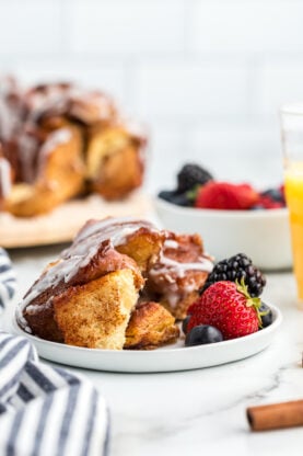Cinnamon roll monkey bread ready to serve on a white plate with fresh berries and orange juice