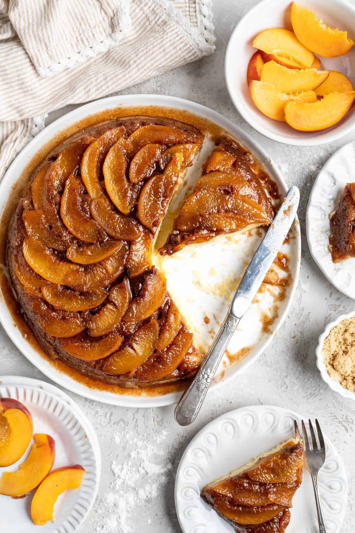 A peach upside down cake with slices placed on plates nearby