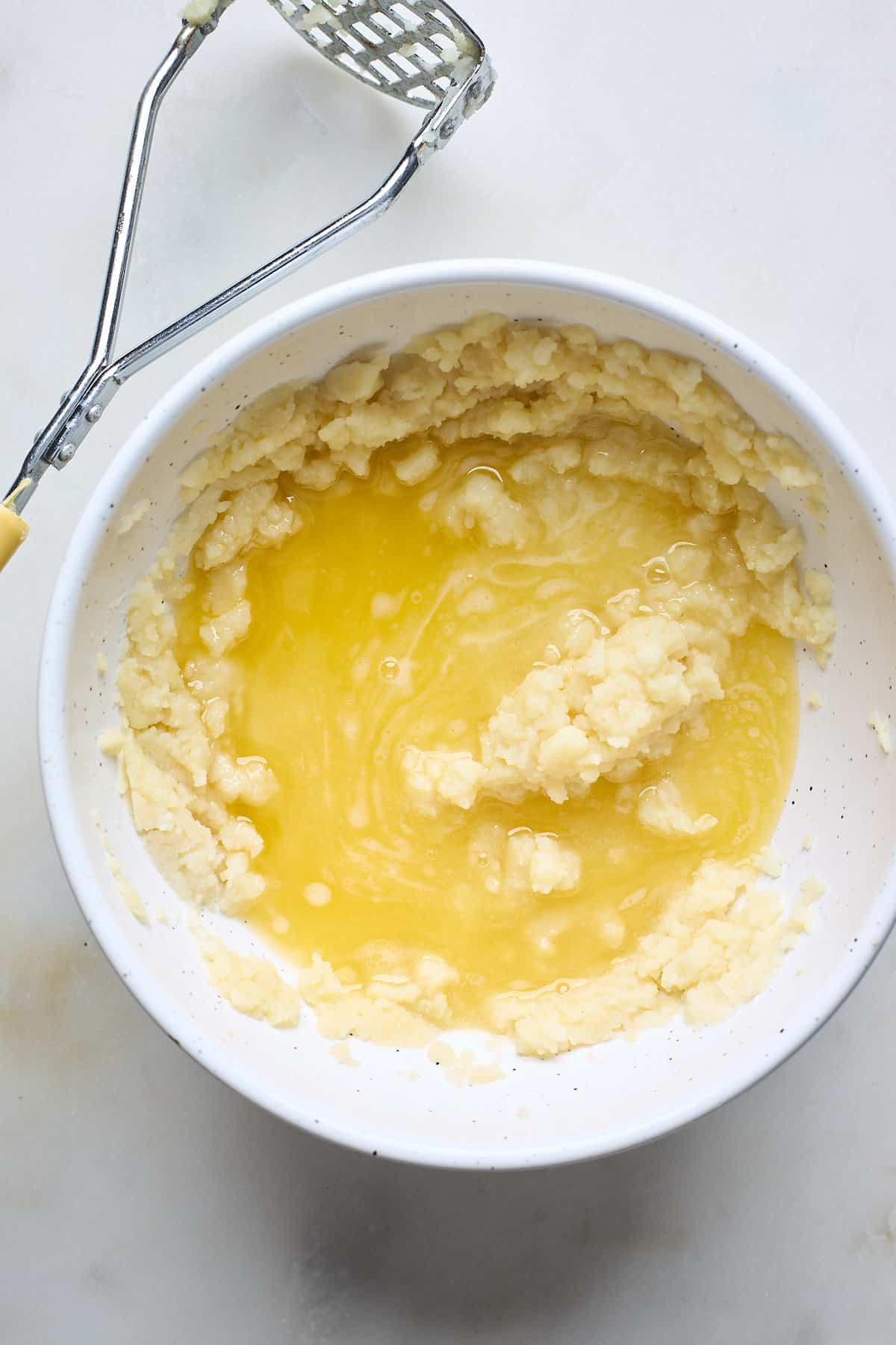 Mashed potatoes and melted butter in a large white bowl