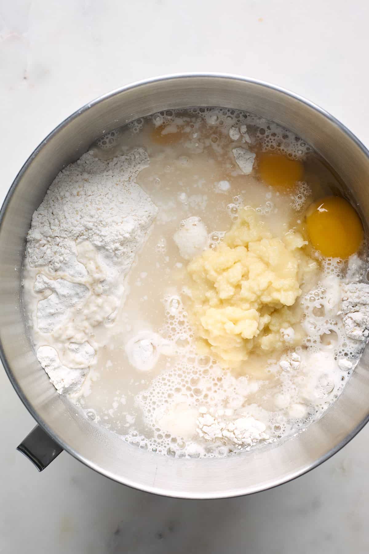 Mashed potato mixture with eggs and water in the bowl of a stand mixer