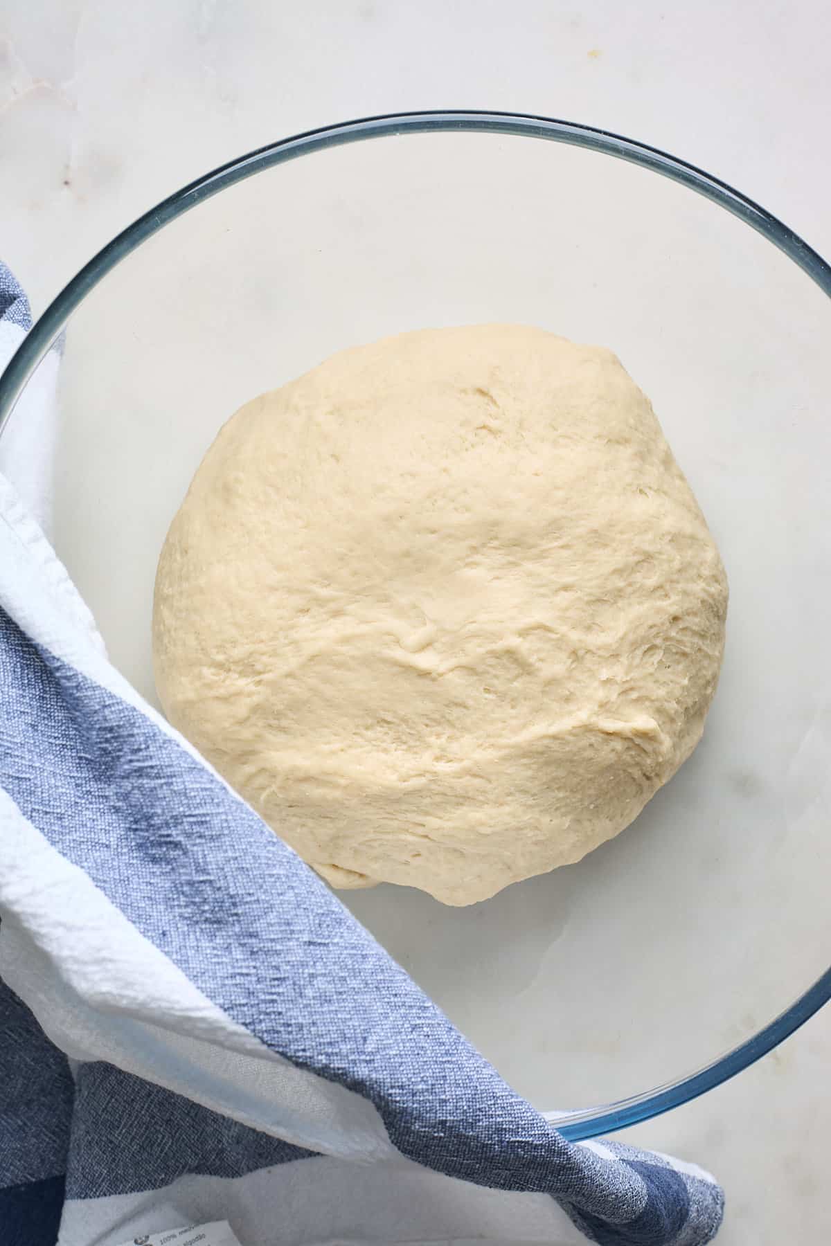 A yeasted dough in a bowl with a towel on top