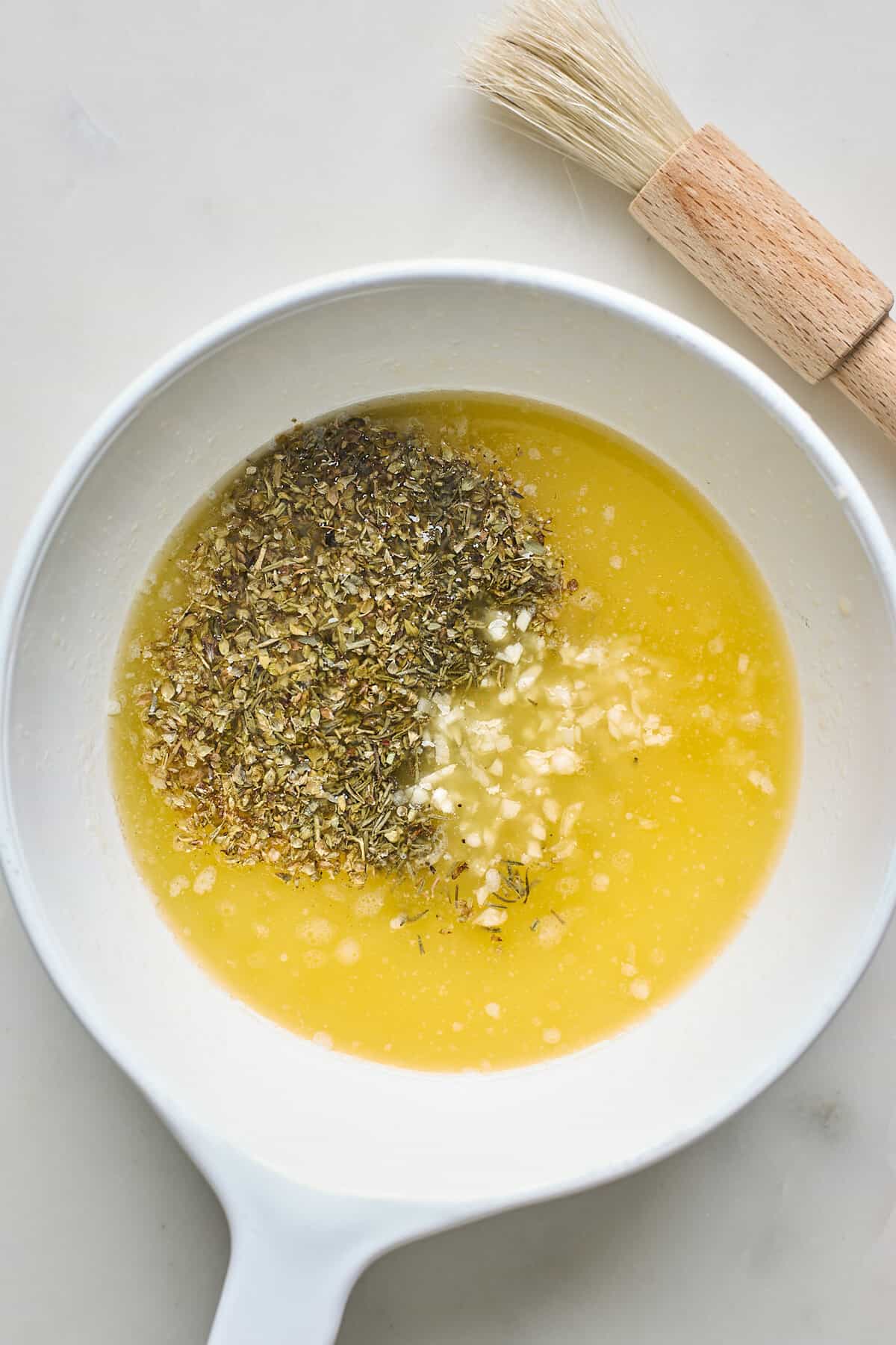 Melted butter, garlic and herbs in a white bowl