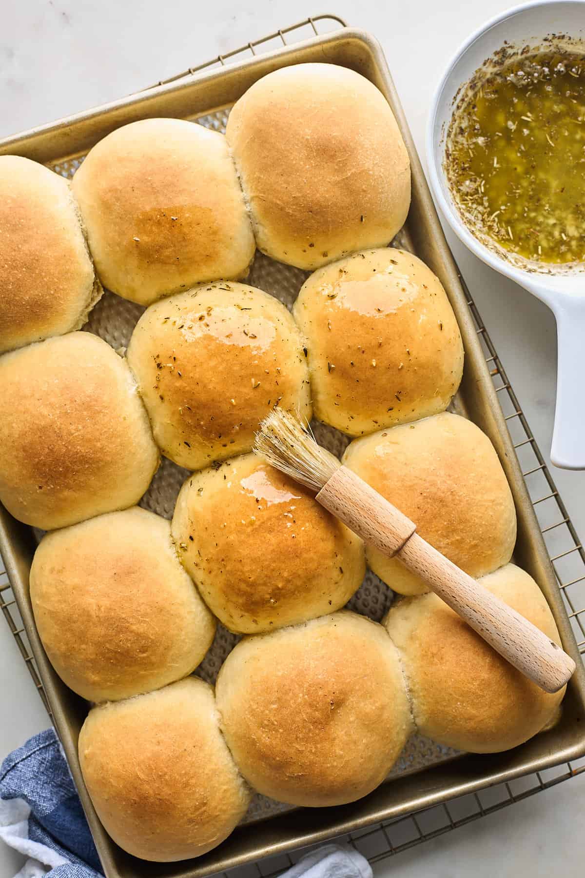 A potato dinner roll recipe out of the oven with a brush adding herby butter glaze