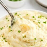 A spoon of mashed potatoes with melty butter being lifted from a bowl