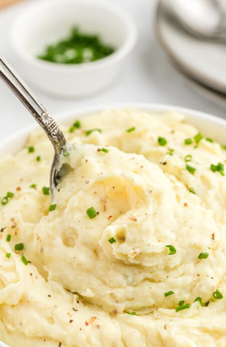 A spoon of mashed potatoes with melty butter being lifted from a bowl
