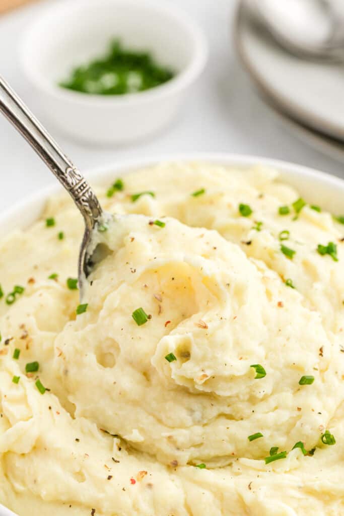 A spoon of sour cream mashed potatoes being lifted from a bowl.