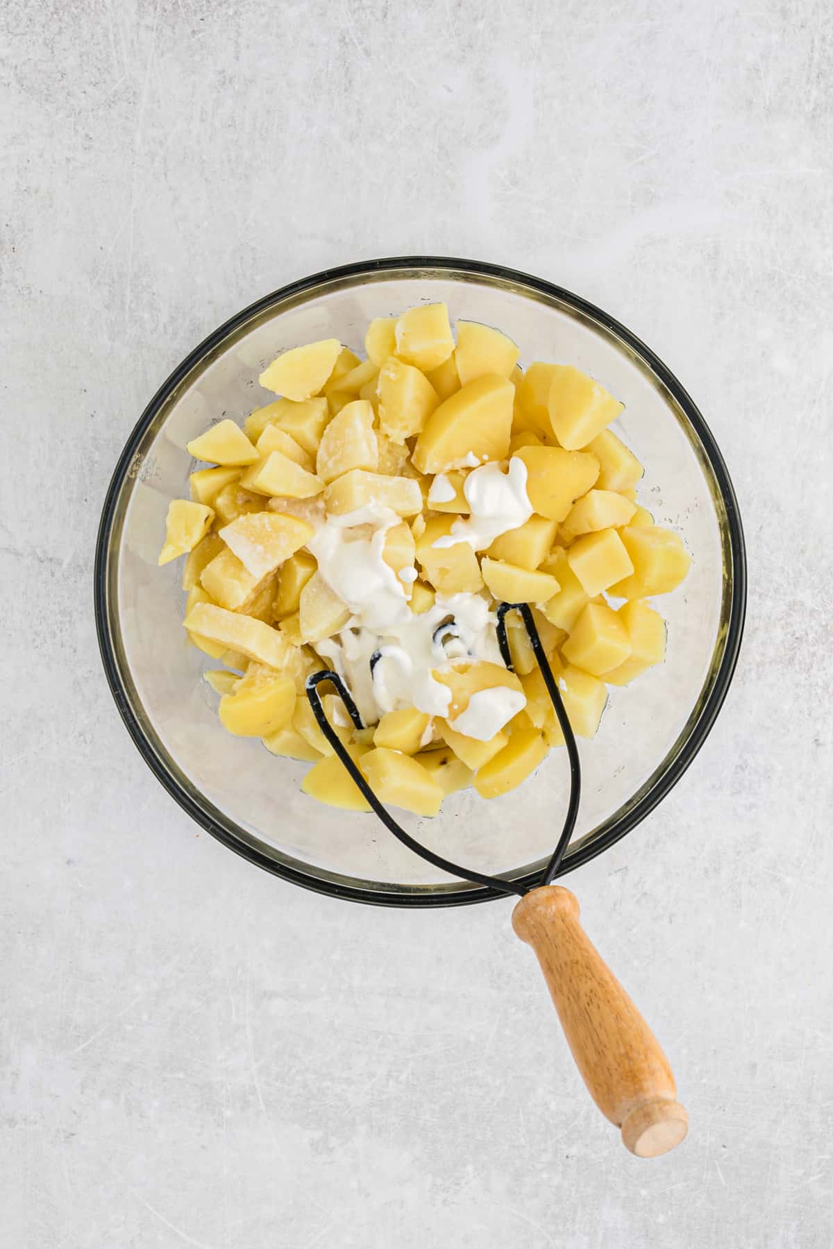 Potato cubes in a clear bowl with a masher