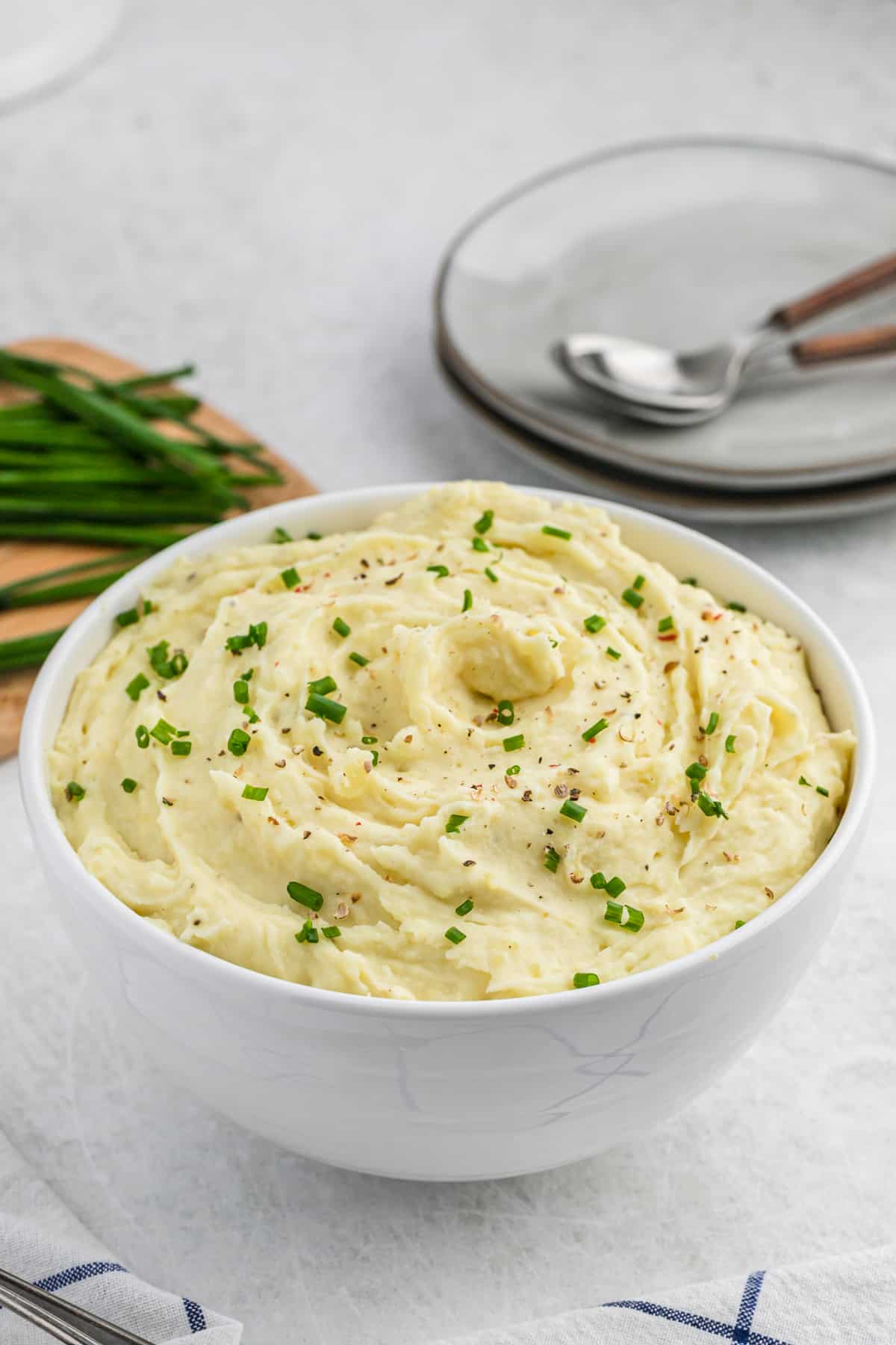 A large serving bowl of sour cream mashed potatoes with plates behind it to serve with