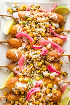 Elote corn dogs with corn topping and pickled onion and lime wedges