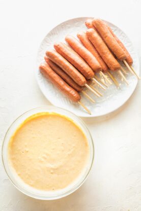 Cornmeal mixture in a bowl with hot dogs on skewers