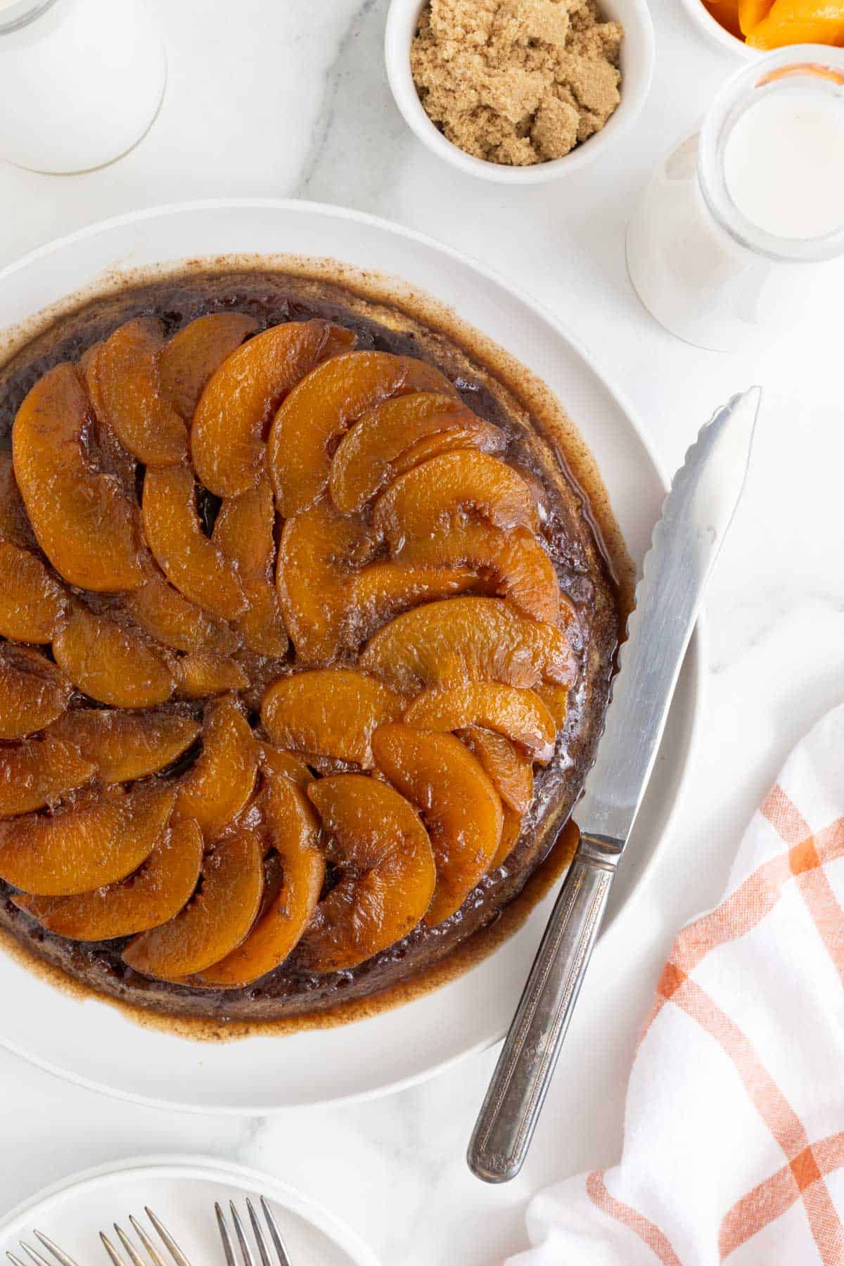 Overhead shot of a whole peach upside down cake surrounded by ingredients like brown sugar and milk
