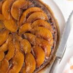 Overhead shot of a whole peach upside down cake surrounded by ingredients like brown sugar and milk