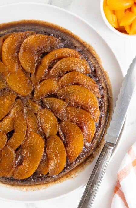 Overhead shot of a whole peach upside down cake surrounded by ingredients like brown sugar and milk