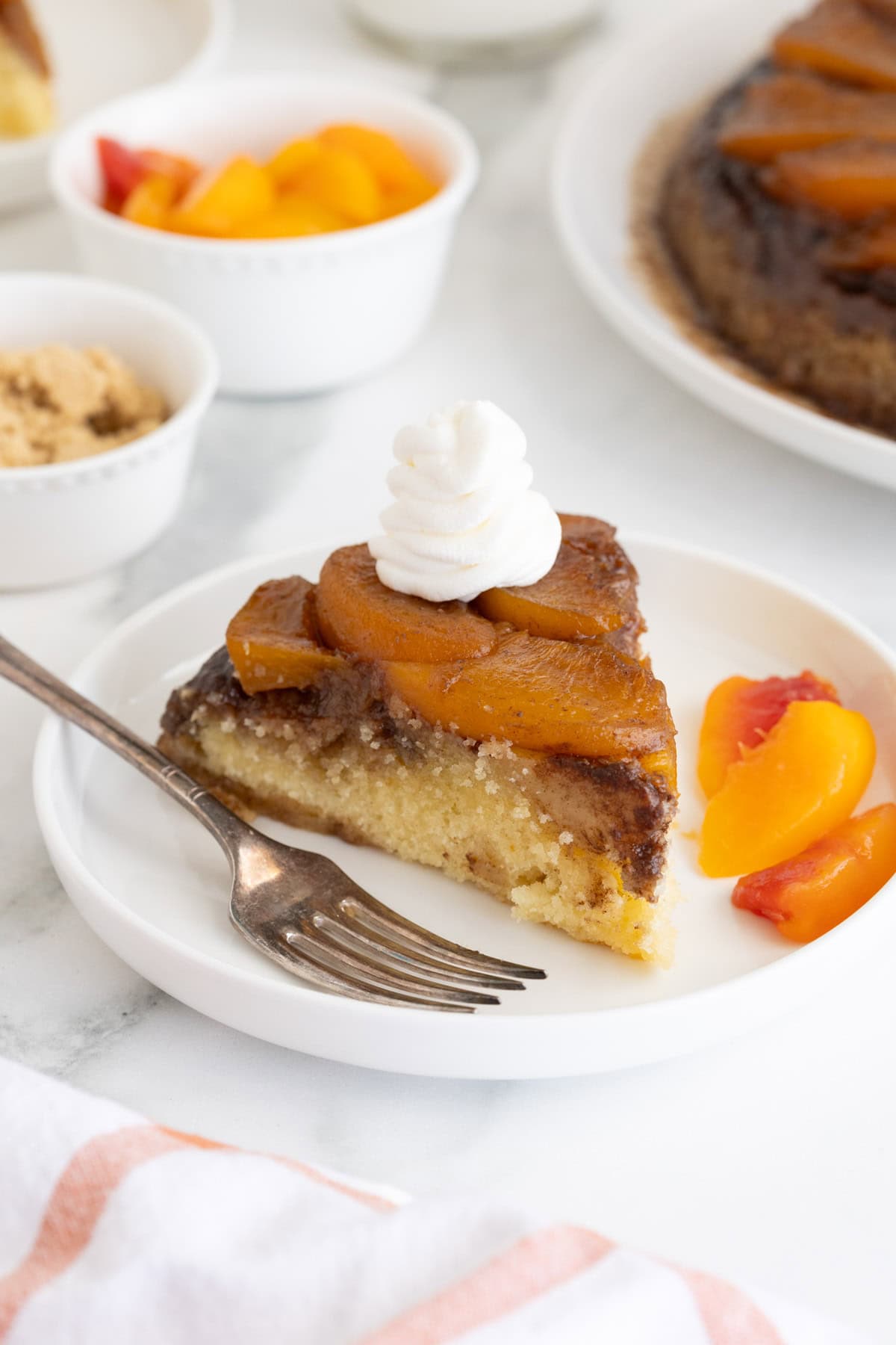 Plated slice of peach upside down cake topped with whipped cream and served with extra peach slices on the side