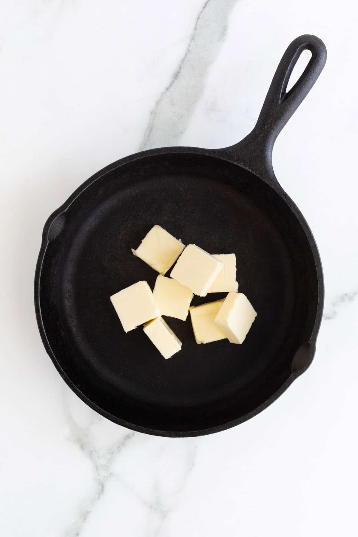 Cubed butter in a black cast iron skillet on a marble surface