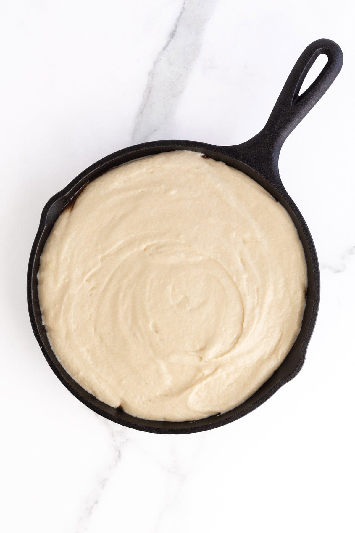 Cake batter spread evenly into a cast iron skillet