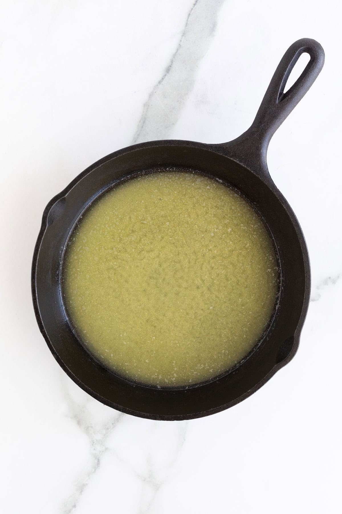 Melted butter in a black cast iron skillet on a white marble countertop