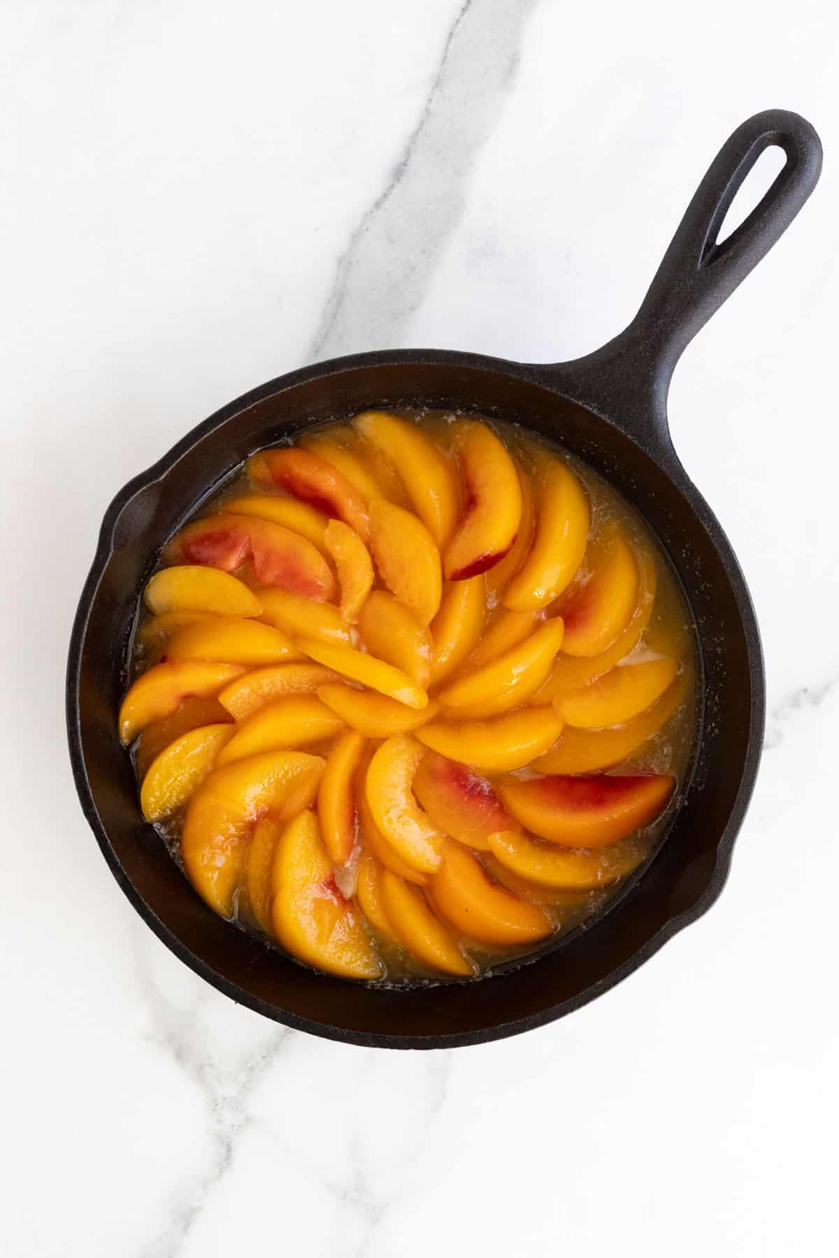 Sliced peaches arranged in a circular pattern over melted butter in a skillet