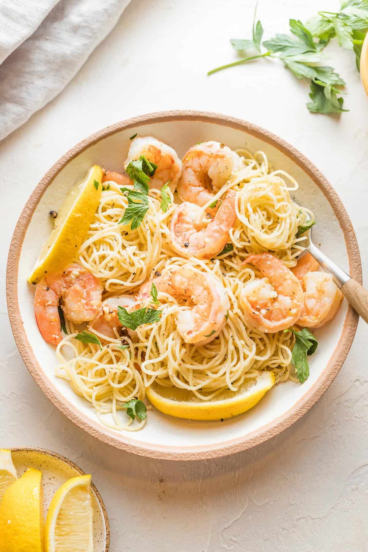 An easy shrimp scampi in a white bowl with a fork and lemon wedges on top