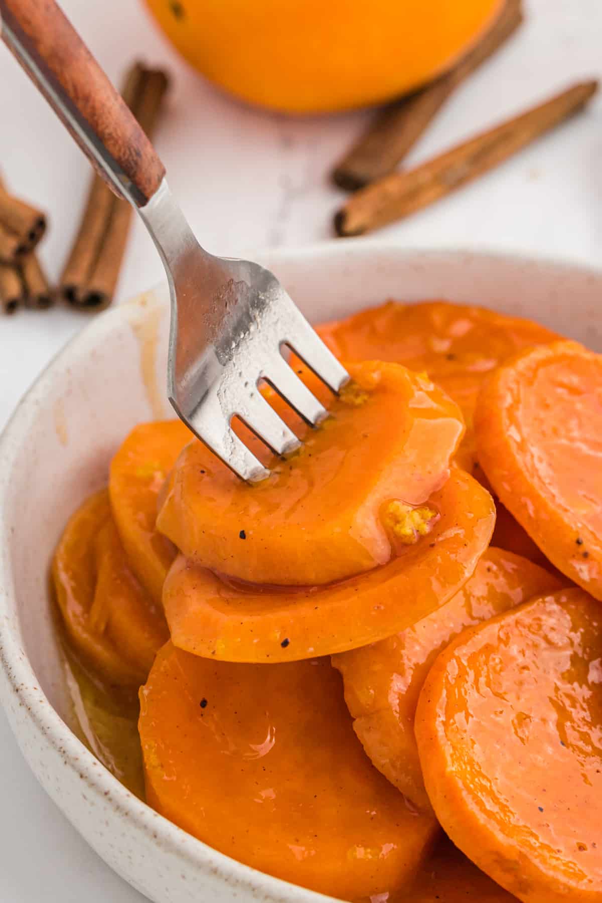 A fork in a bowl of sliced candied yams.