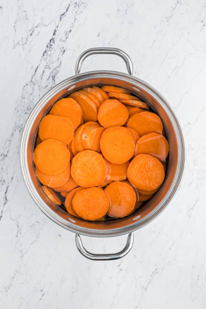 Sliced yams in a saucepan with water on white countertop